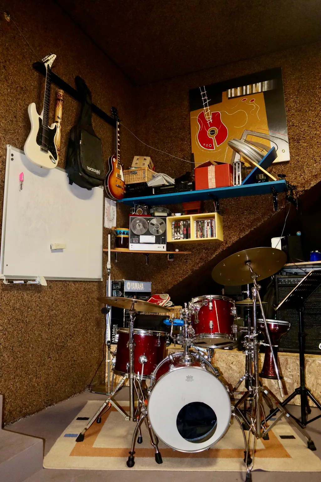 Bateria no estúdio, com guitarras e material de estudo ao fundo